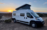 Witness a stunning sunset from this Winnebago Solis pop-top camper van, ideal for your next RV rental adventure on rugged terrain.
