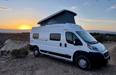 Witness a stunning sunset from this Winnebago Solis pop-top camper van, ideal for your next RV rental adventure on rugged terrain.