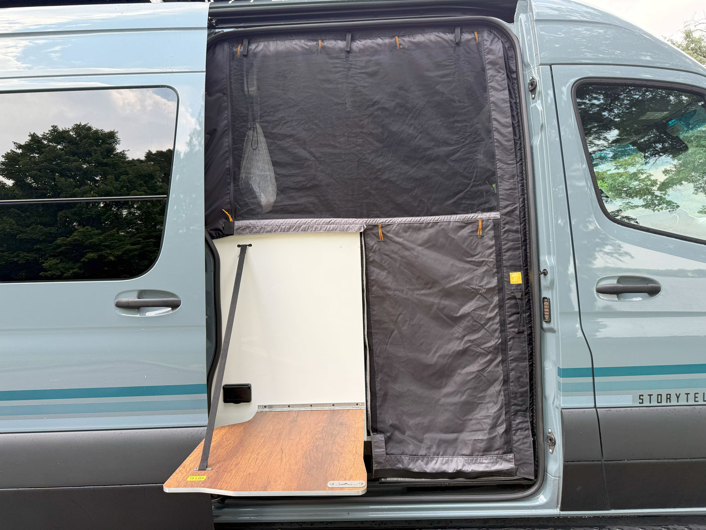 Open side door of a light blue Storytel van, showcasing a pull-out table and protective mesh screen. Perfect for your rv rental.