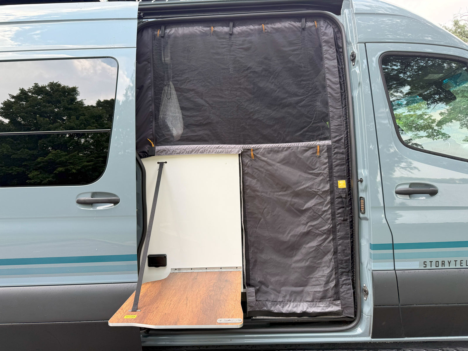 Open side door of a light blue Storytel van, showcasing a pull-out table and protective mesh screen. Perfect for your rv rental.