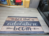 "Let the adventure begin" mat on a light wood-look floor inside an RV rental, with storage nets and a seat.
