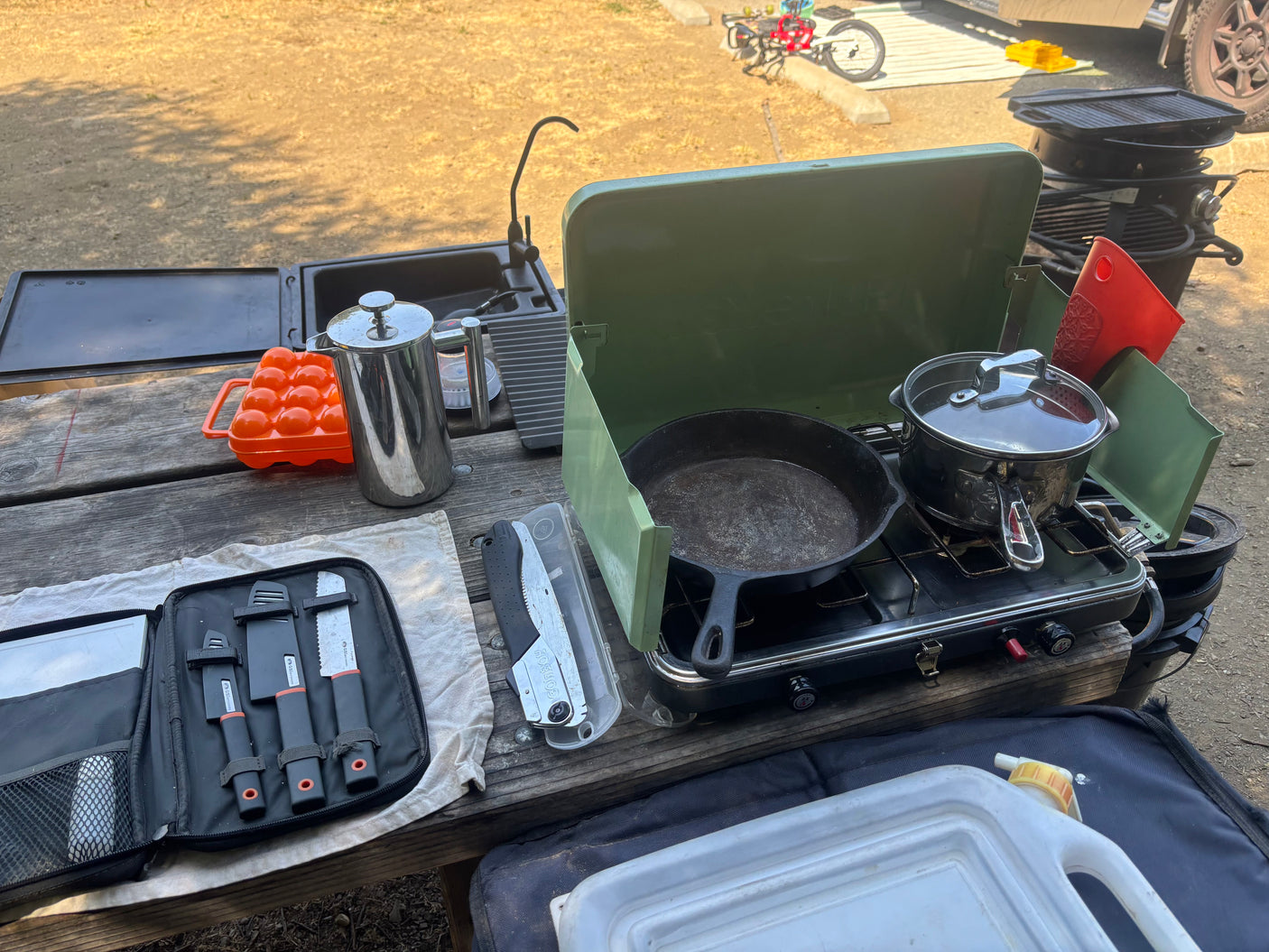 An RV rental's portable camping kitchen setup on a picnic table, featuring a sink, stove, cookware, and various tools.