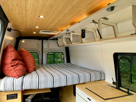 Stylish RV rental interior: light wood ceiling, comfy bed, smart storage, and compact kitchen. Perfect for van life!