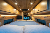 Cozy RV rental interior showcasing a large bed, elegant wood paneling, overhead storage, and integrated lighting.