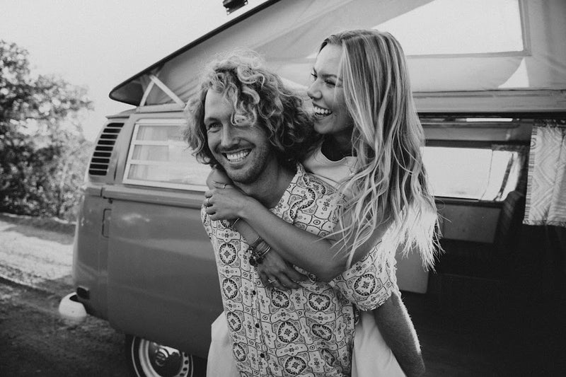 A happy couple on an RV rental trip. The man gives the woman a piggyback ride in front of their classic pop-top campervan. — photo 20