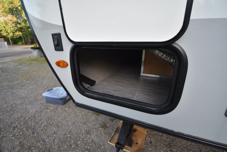 Open storage on an RV rental, showing a large exterior compartment with light interior flooring. An orange marker light & switch are visible.