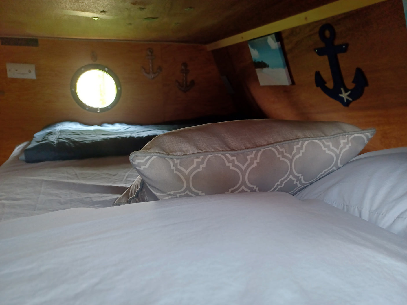 Cozy RV rental interior: bed with patterned pillow, porthole, and charming nautical decor.