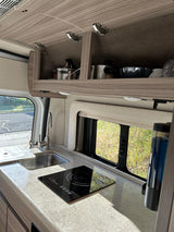 Compact RV rental kitchen with sink, induction cooktop, and overhead storage for easy travel meals.