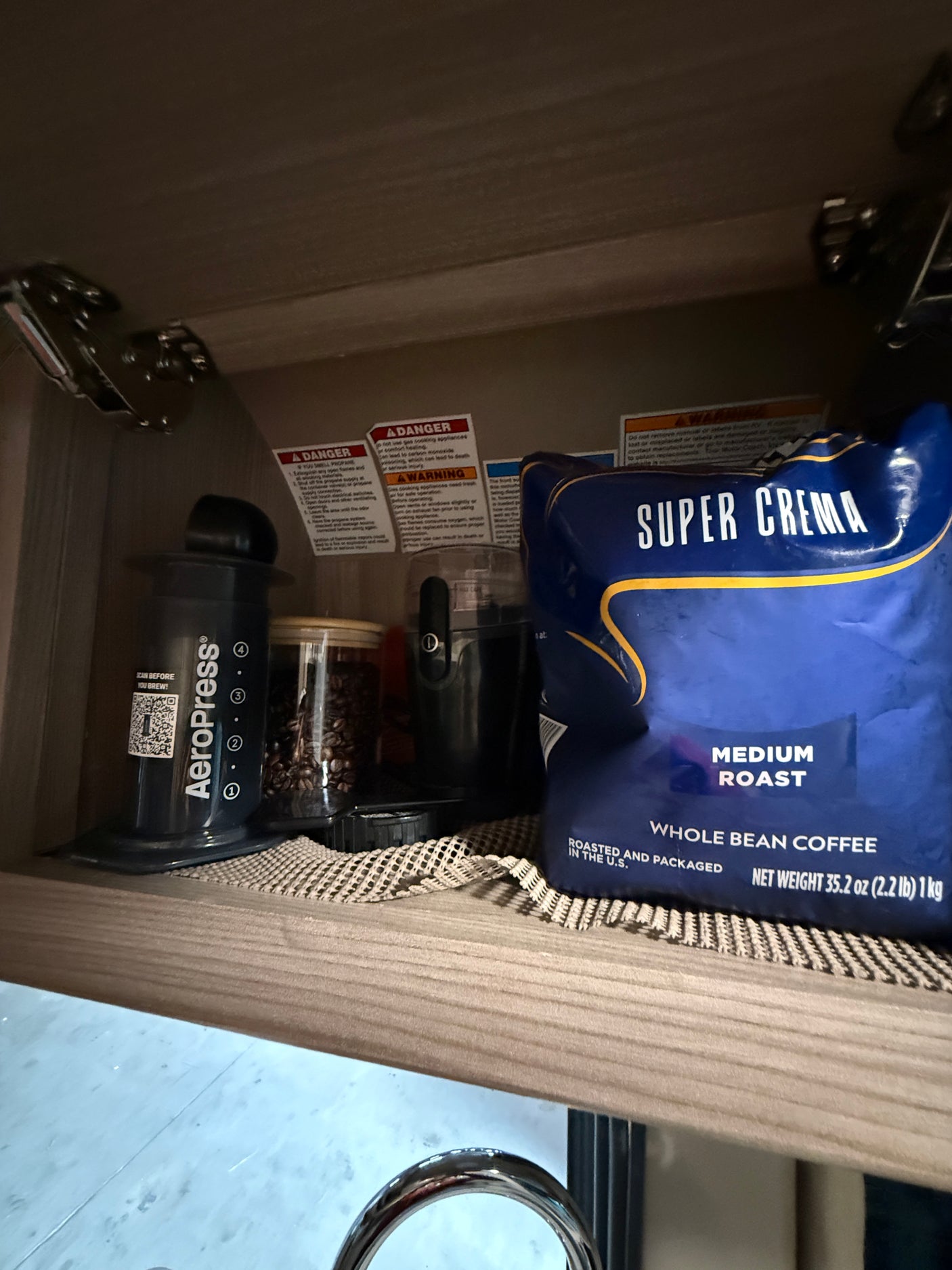 Convenient RV rental coffee setup: AeroPress, grinder, whole beans, and Super Crema coffee stored in an overhead cabinet.
