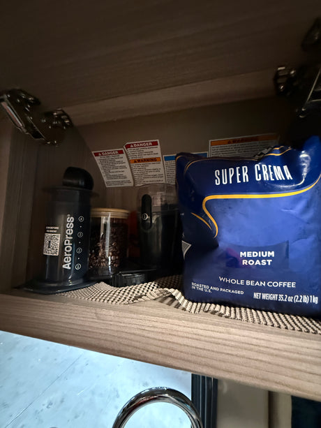 Convenient RV rental coffee setup: AeroPress, grinder, whole beans, and Super Crema coffee stored in an overhead cabinet.