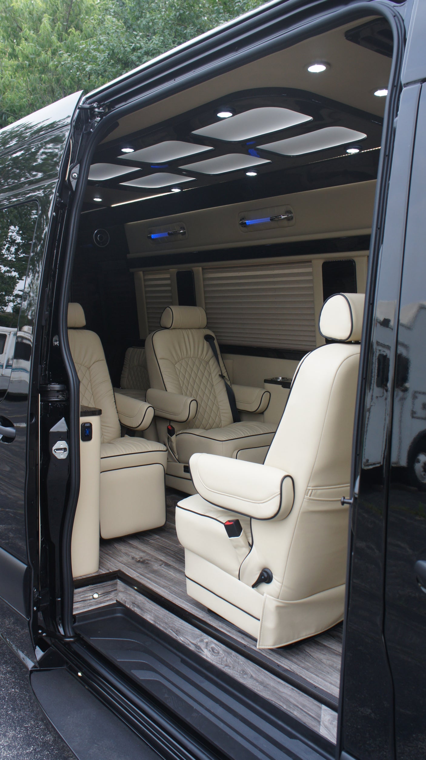RV rental: Luxurious custom van interior with cream leather captain's chairs, wood floor, and ambient lighting.