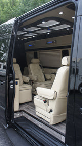 RV rental: Luxurious custom van interior with cream leather captain's chairs, wood floor, and ambient lighting.
