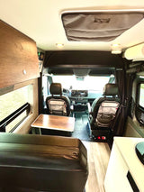 This RV rental interior offers a dining table, kitchen, and comfortable seating, looking towards the front cabin.