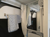 Inside an RV rental shower area: blue towels on a bar, a white shower curtain, and a mirror reflecting the space and a shower head.