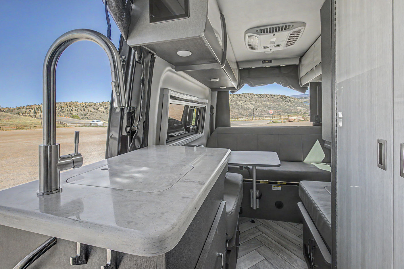 Explore this modern RV rental kitchen & dinette, featuring a sleek faucet, marbled counter, and ample storage for travel.