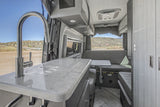 Explore this modern RV rental kitchen & dinette, featuring a sleek faucet, marbled counter, and ample storage for travel.