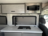 Inside an RV rental: a modern compact kitchen with a sink, induction cooktop, Contoure microwave, and grey storage cabinets.