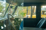 From inside a vintage Land Rover, viewing other yellow RV rentals and Land Rovers parked among fall trees in a forest.