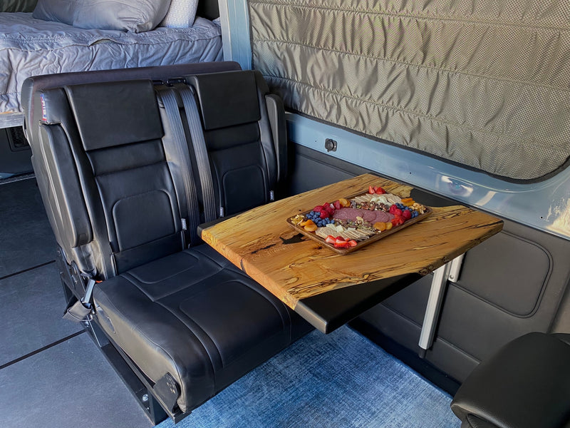 Enjoy comfort in this RV rental: two black seats, a wood table with charcuterie, and bed space. Perfect for travel! — photo 10