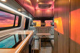 Step inside this luxury RV rental, featuring a sleek kitchen, cozy seating with a table, and vibrant sunset views.