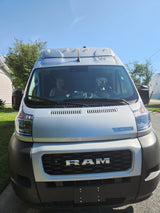Front view of a light Winnebago Ram van, ideal for RV rental, with a dog "driving" and a person visible inside.