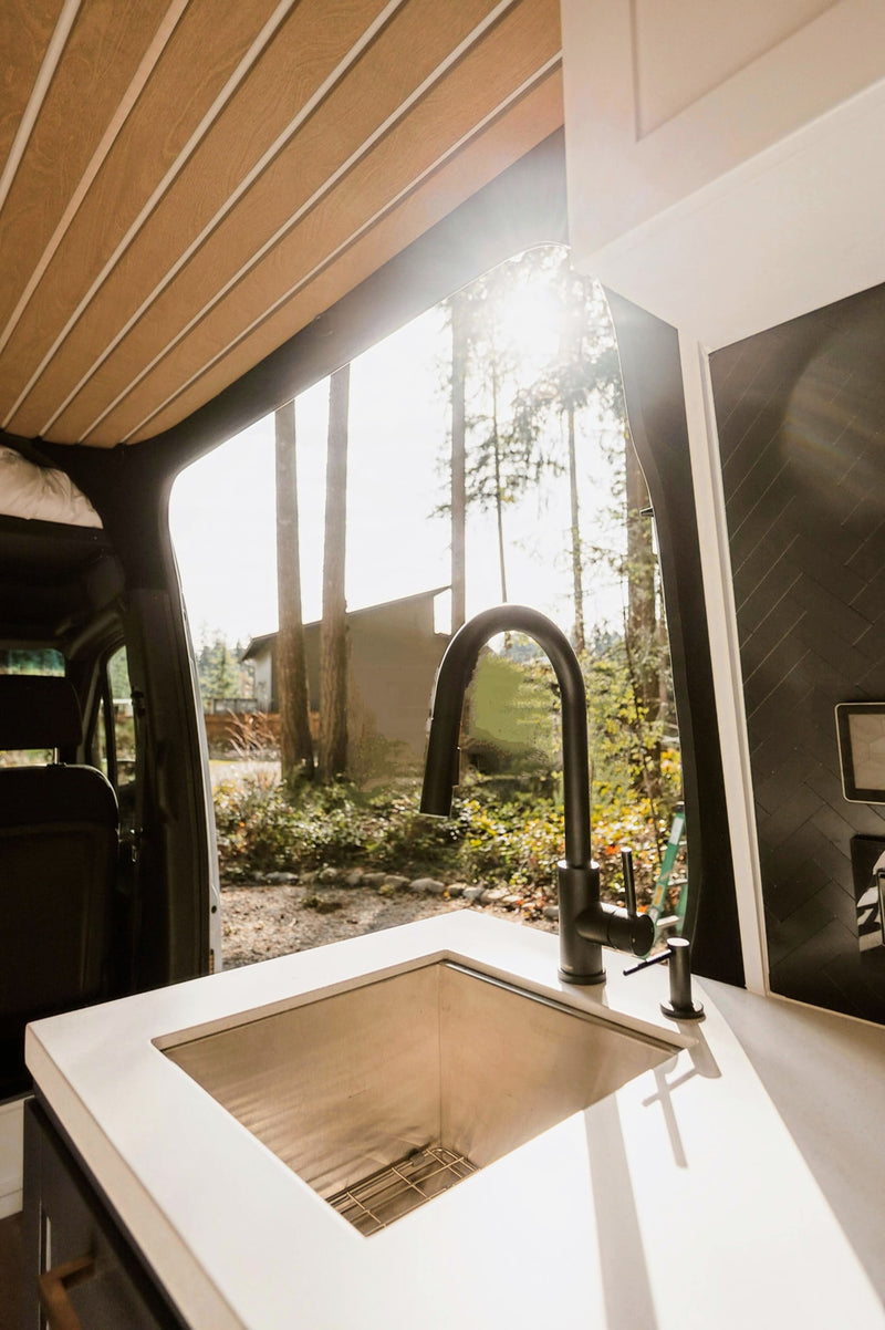 Spacious RV rental interior with a sleek stainless steel sink, black faucet, and bright forest views. — photo 19
