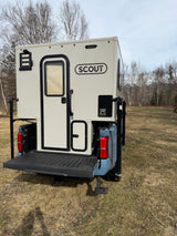 Rear of a Scout truck camper mounted on a blue pickup truck in a grassy field. Consider this RV rental for your next adventure.