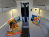 Modern RV rental interior featuring cozy seating, artistic Van Gogh pillows, overhead storage, and warm lighting for comfortable travel.