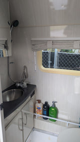 This compact rv rental bathroom features a sink, extendable shower, window, and toiletries on a shelf. Ready for your next adventure.
