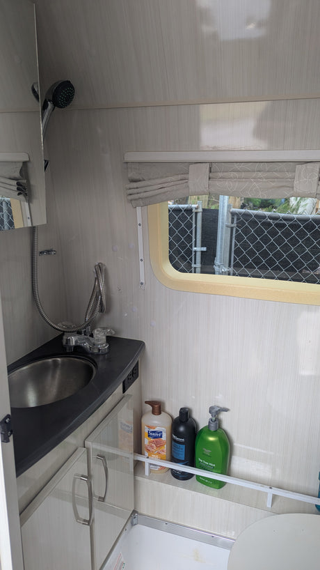 This compact rv rental bathroom features a sink, extendable shower, window, and toiletries on a shelf. Ready for your next adventure.