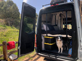 Pet-friendly rv rental with rear doors open, showing a cozy bed and storage. A dog stands inside, ready for outdoor adventure.