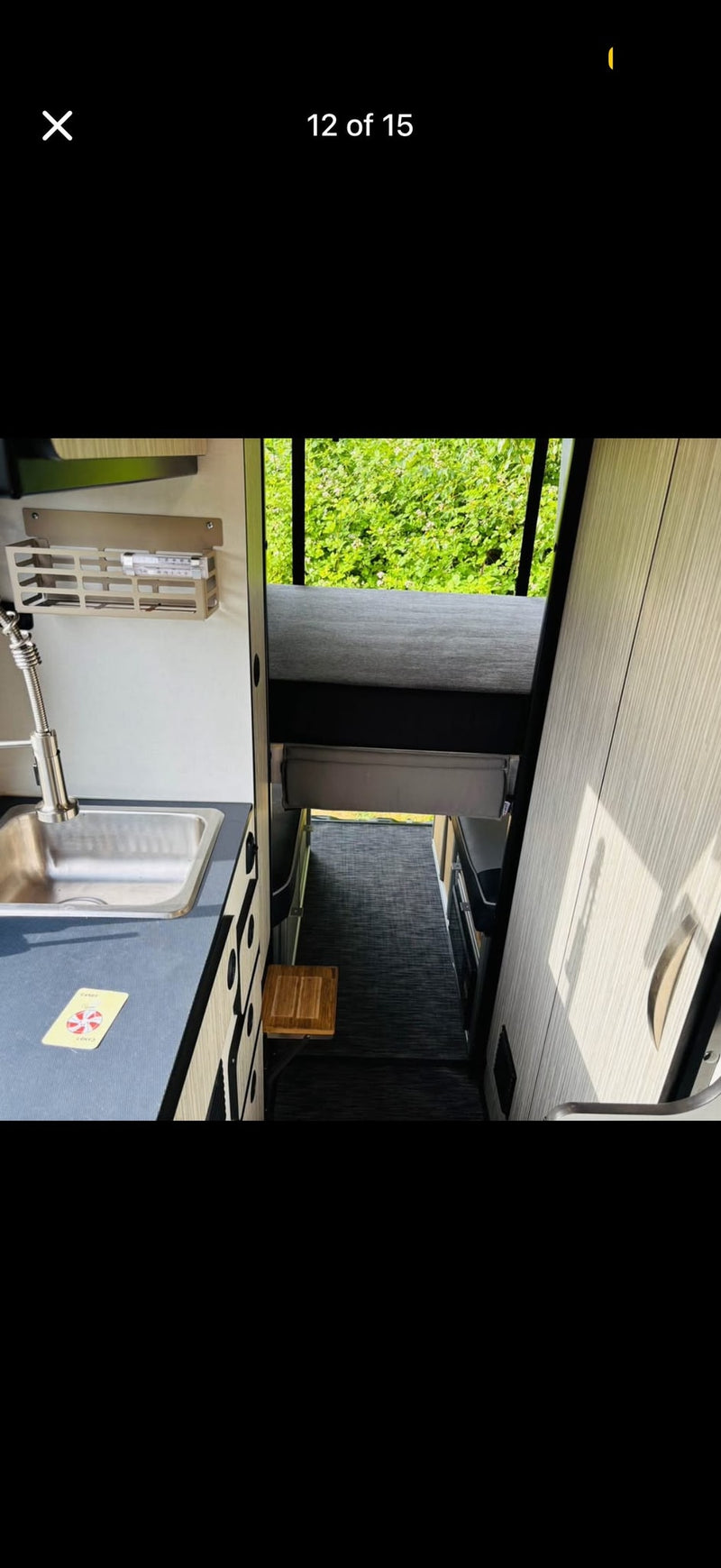 RV rental interior showing a compact kitchen with sink, storage, and a thermometer, plus an upper bed and narrow walkway. — photo 7