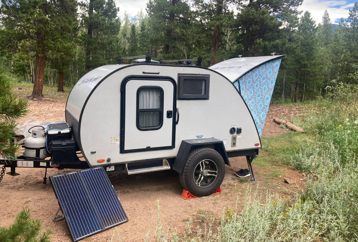 Exploring off-grid with an RV rental travel trailer, featuring solar and a patterned awning amidst trees.