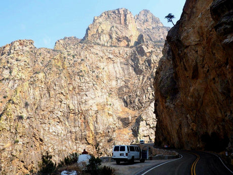 Winding mountain road trip with an rv rental. White van parked by towering rock cliffs on a scenic highway.