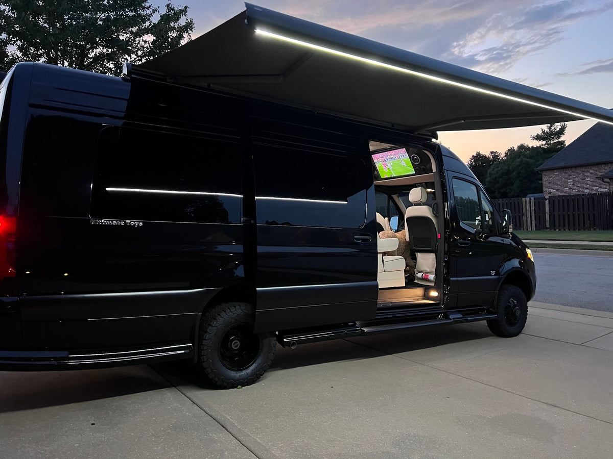Luxury black Sprinter van with lit awning and interior TV showing sports; an excellent rv rental option.|A black Sprinter van