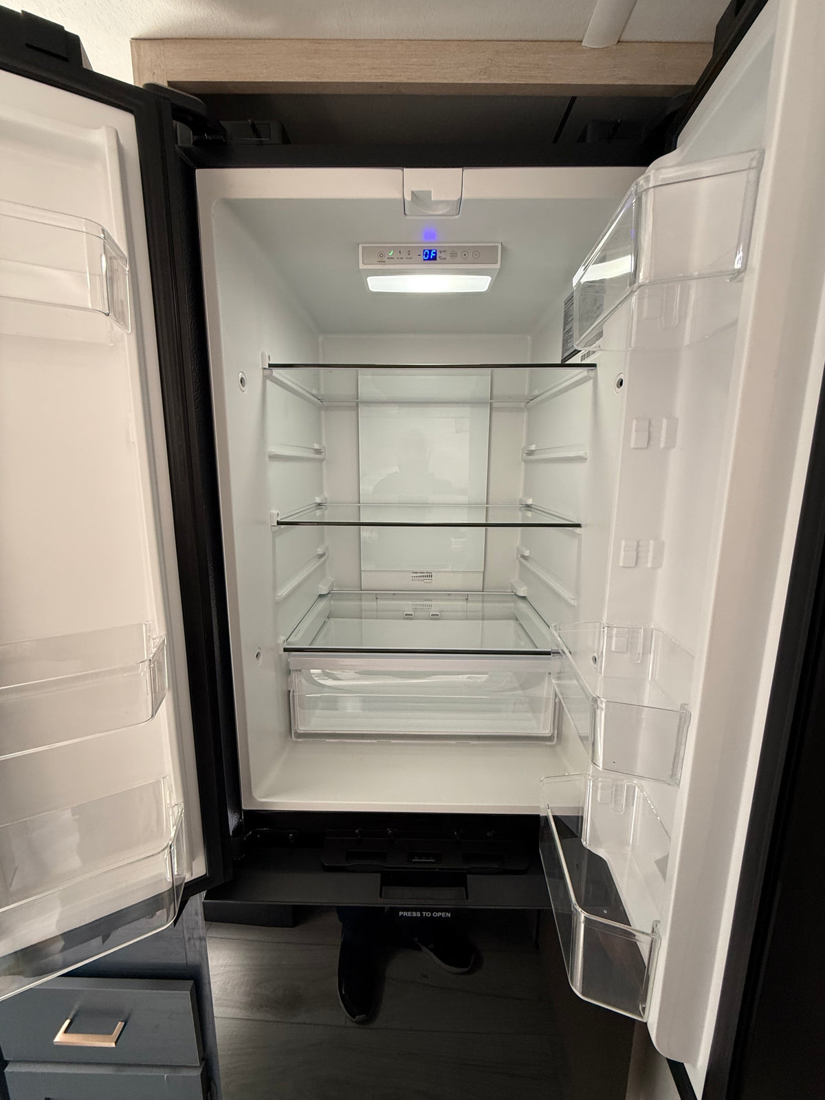 Inside an open, empty RV rental refrigerator, featuring clear glass shelves, plastic door bins, and a digital control panel. — photo 6