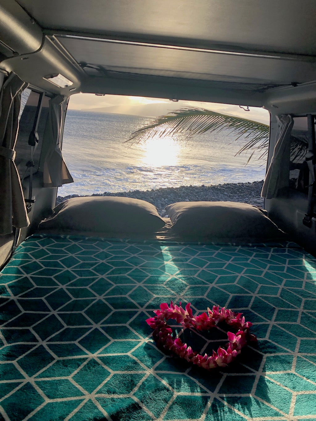 Cozy rv rental bed, heart lei on teal blanket, sunny ocean view with palm frond from van. Beachfront bliss. — photo 16