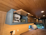 Modern rv rental interior: bamboo walls, ceiling, & storage cabinet with towels, grey overhead units, cozy bed, and window view.