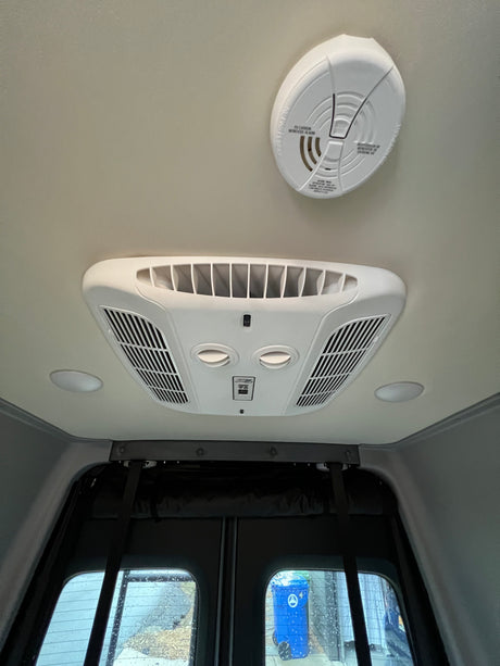 RV rental ceiling: AC unit, carbon monoxide alarm, recessed lights, and window view outside a vehicle.
