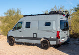 Gray Winnebago Revel 4x4 camper van on a dirt path in a desert landscape, ideal for an rv rental adventure.