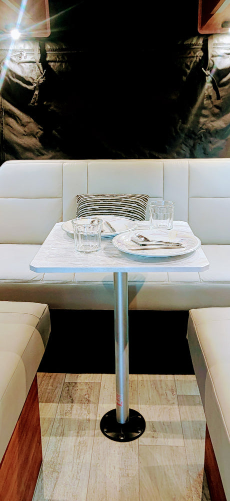 RV rental dinette: Clean white benches, set table with glasses & plates, ready for meals in a modern interior.