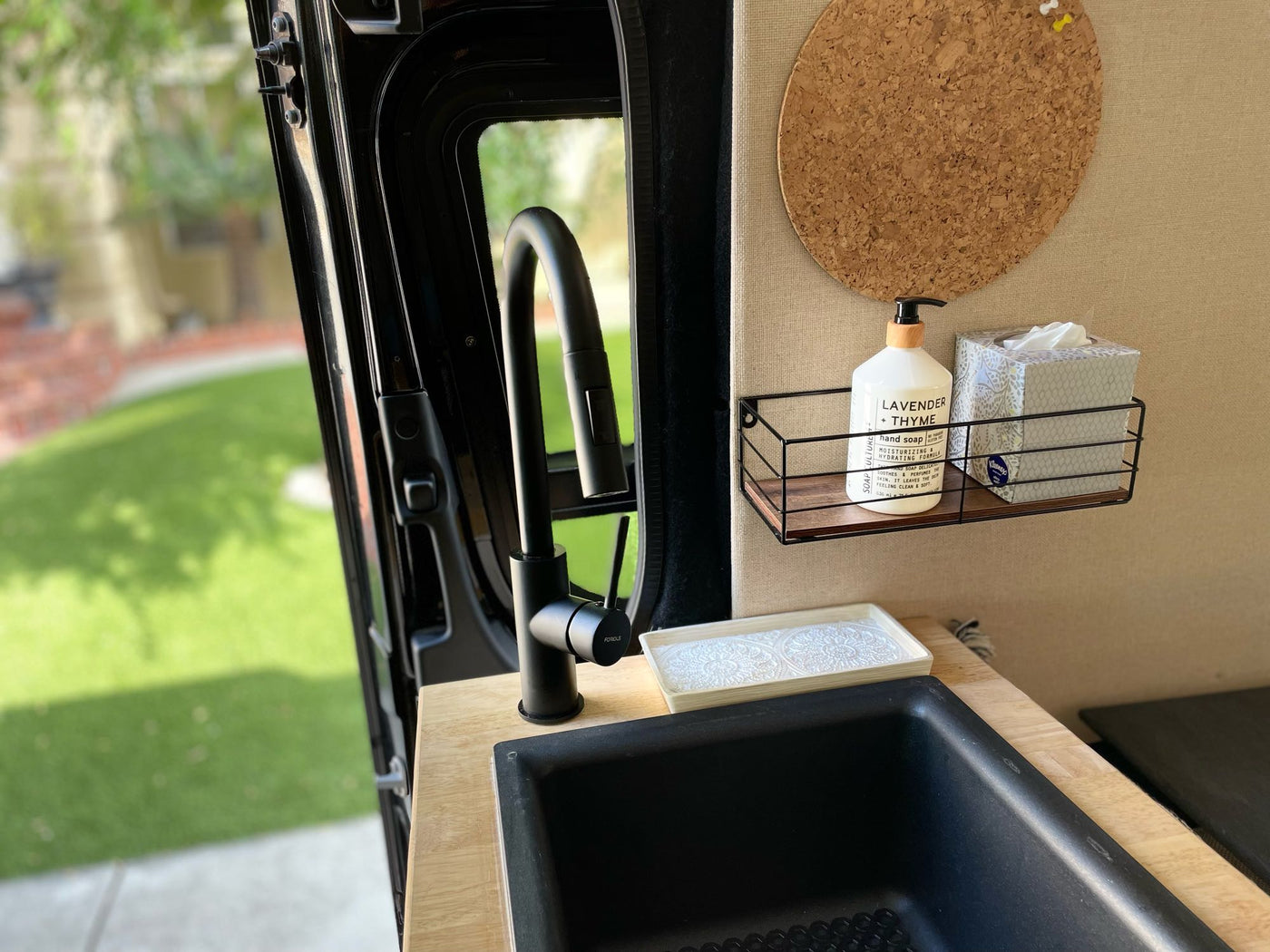 A compact kitchen in an RV rental, featuring a black sink, faucet, soap, tissues, and corkboard. — photo 13