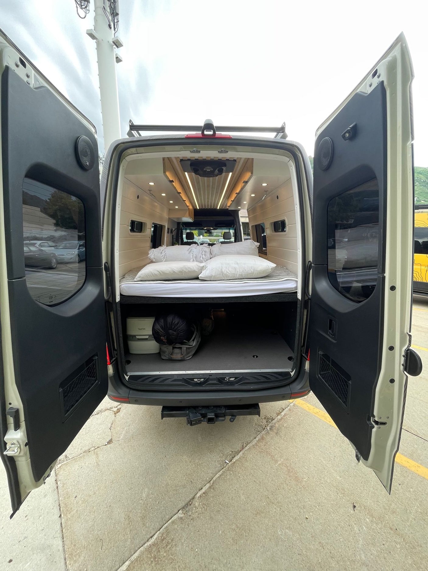 Open doors reveal a cozy bed & storage in this white camper van, ready for your RV rental adventure.