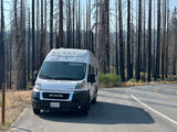 Scenic rv rental road trip stop: a white camper van parked by charred trees in a post-wildfire forest. California travel.