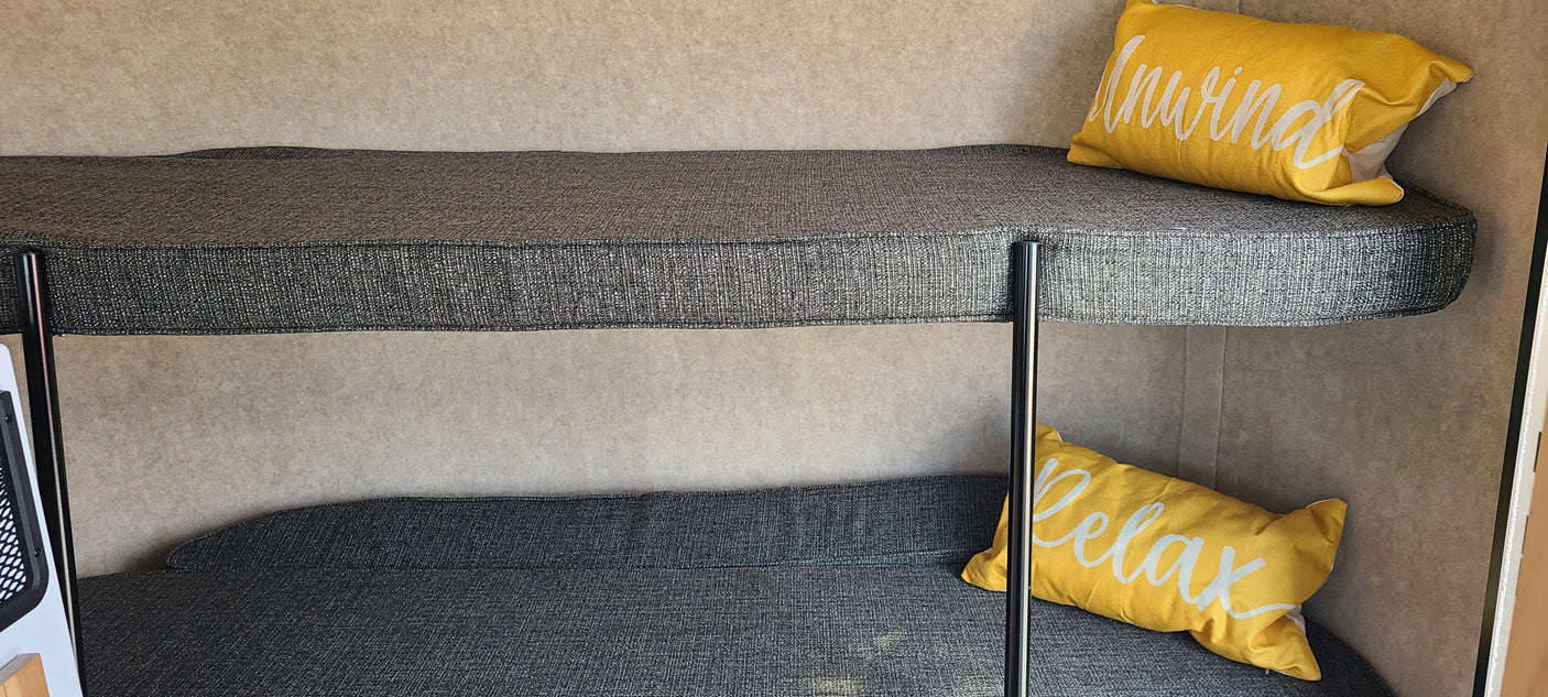 RV rental bunk beds: a cozy sleeping area with grey cushions, light walls, and yellow "Unwind" & "Relax" pillows.