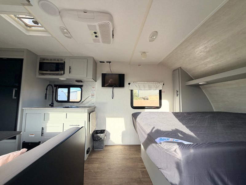Clean rv rental interior. Features a compact kitchen with microwave, sink, TV, and a neatly made bed. Bright and airy. — photo 8