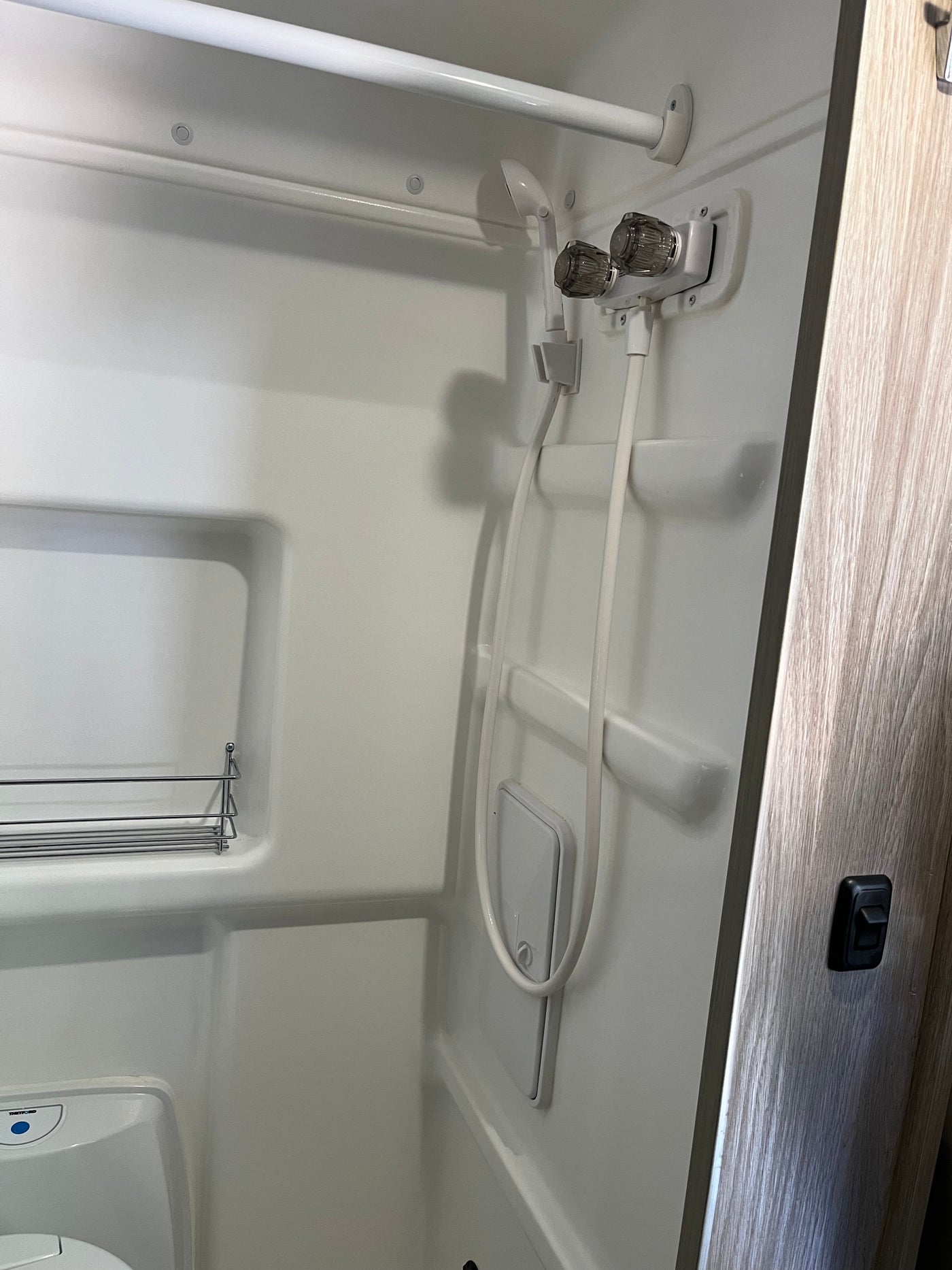 Compact shower and toilet area inside an RV rental, featuring a handheld shower, control knobs, and a small shelf. — photo 16