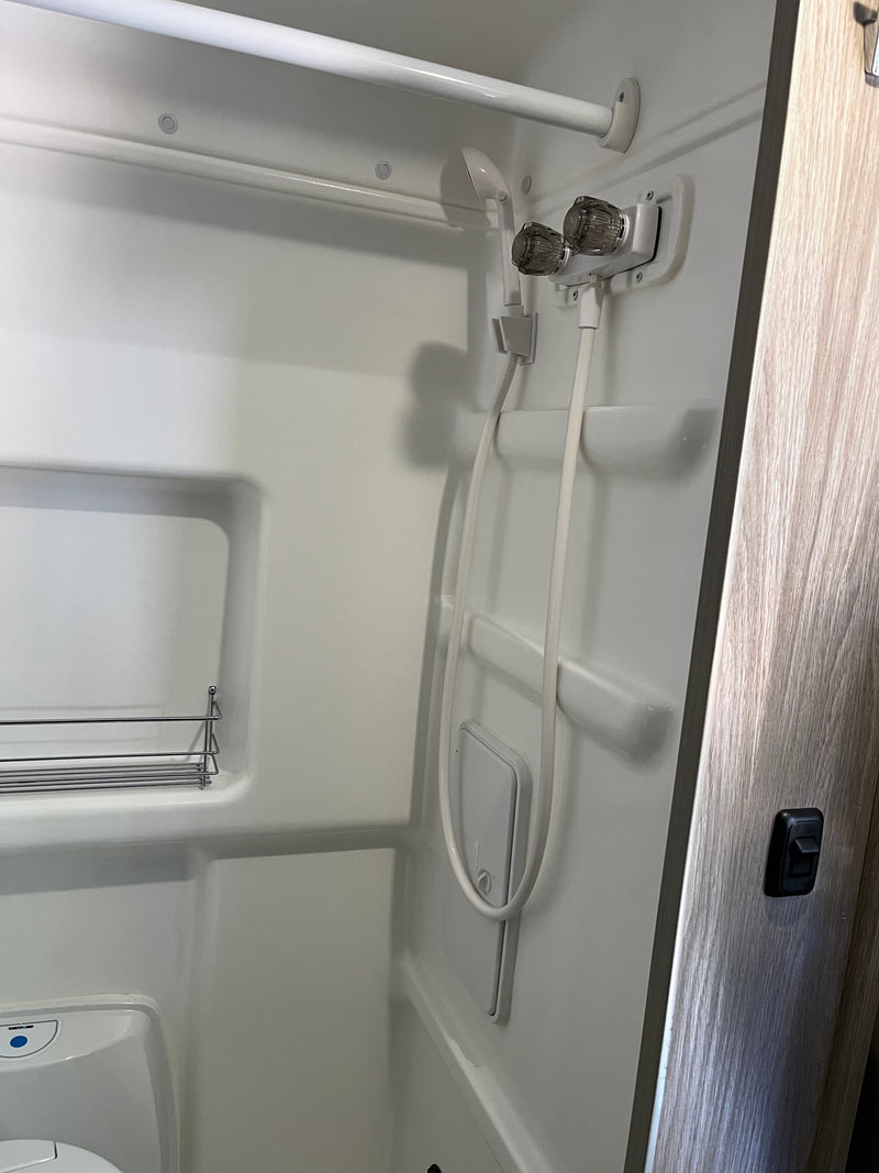 Compact shower and toilet area inside an RV rental, featuring a handheld shower, control knobs, and a small shelf. — photo 16