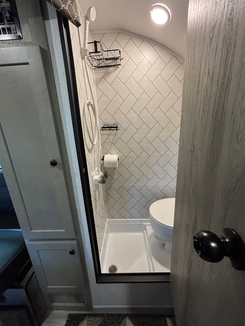 Compact RV rental wet bath featuring a shower, toilet, and modern herringbone tiled walls. — photo 14