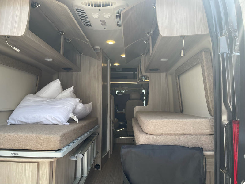 RV rental interior showing two beds, open overhead storage, and an AC unit. Perfect for road trip living. — photo 15